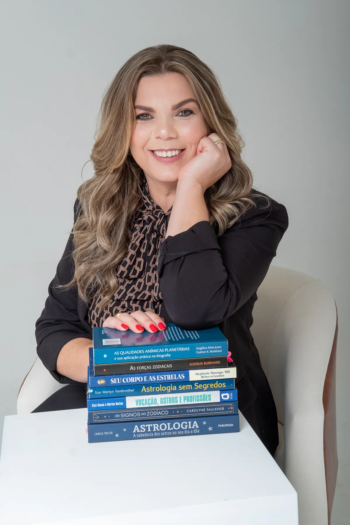 Lucinda de blazer preto apoiada sobre livros de astrologia